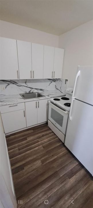 Kitchen featuring white shaker-style cabinetry, high-contrast patterned backsplash, stainless steel sink, electric range, and wood-finish flooring