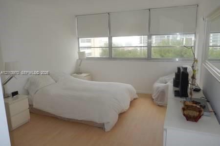 Room featuring wood-finish flooring, a wall-to-wall window configuration, roller shades, and a large wall-mounted mirror