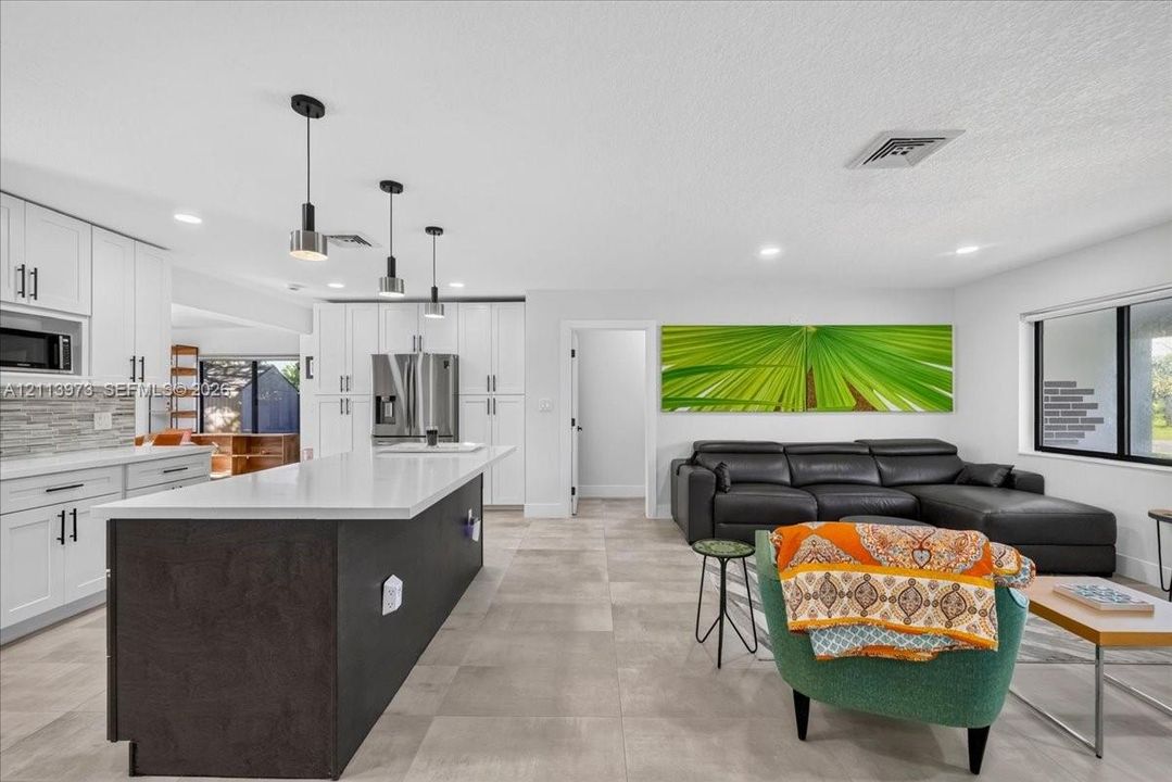 Kitchen featuring white shaker-style cabinetry, an expansive center island with a dark finish, quartz countertops, and a stacked stone backsplash, complemented by large-format tile flooring throughout