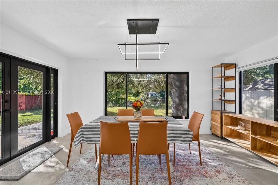 Contemporary geometric chandelier, expansive floor-to-ceiling windows with black frames, wood-finish flooring, and built-in wood shelving units