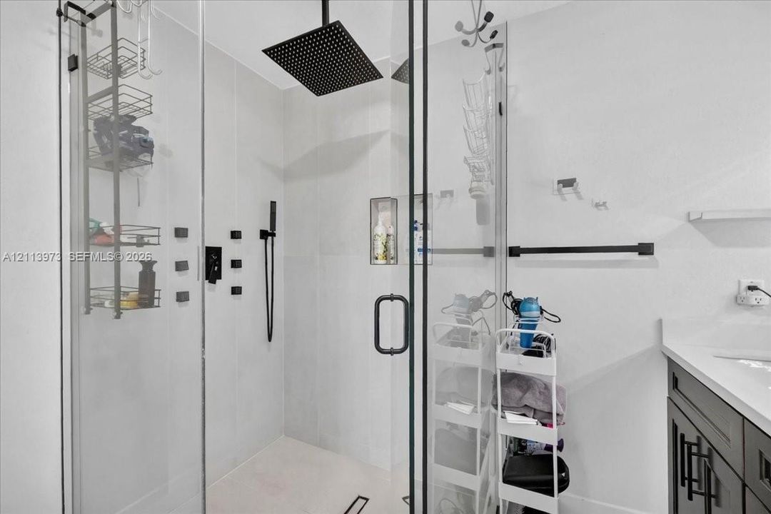 Walk-in shower featuring a frameless glass enclosure, oversized square rainfall showerhead, matte black hardware, integrated tiled niche, and light-toned wall tile