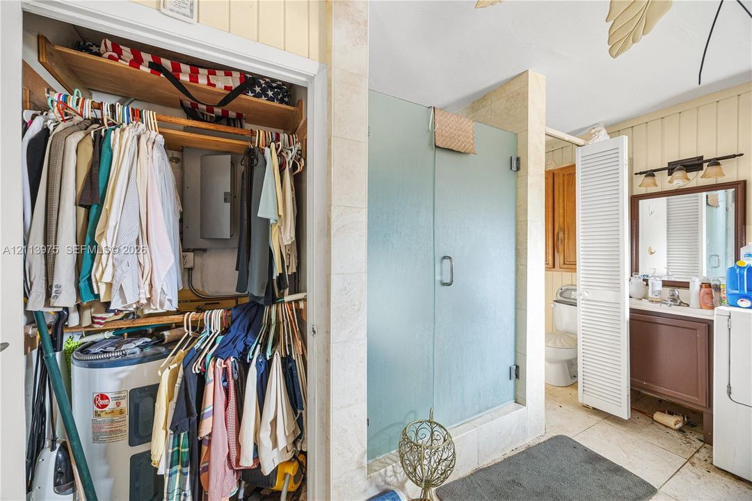 Bathroom featuring a vanity with wood-finish cabinetry, a framed wall mirror, a walk-in shower with frosted glass enclosure, and stone-finish tile flooring
