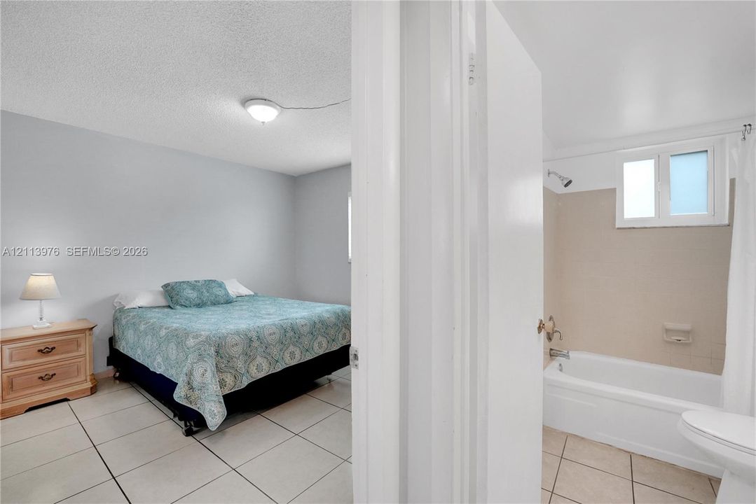 Room featuring large-format ceramic tile flooring and a standard bathtub with a wall-mounted shower fixture and tile surround