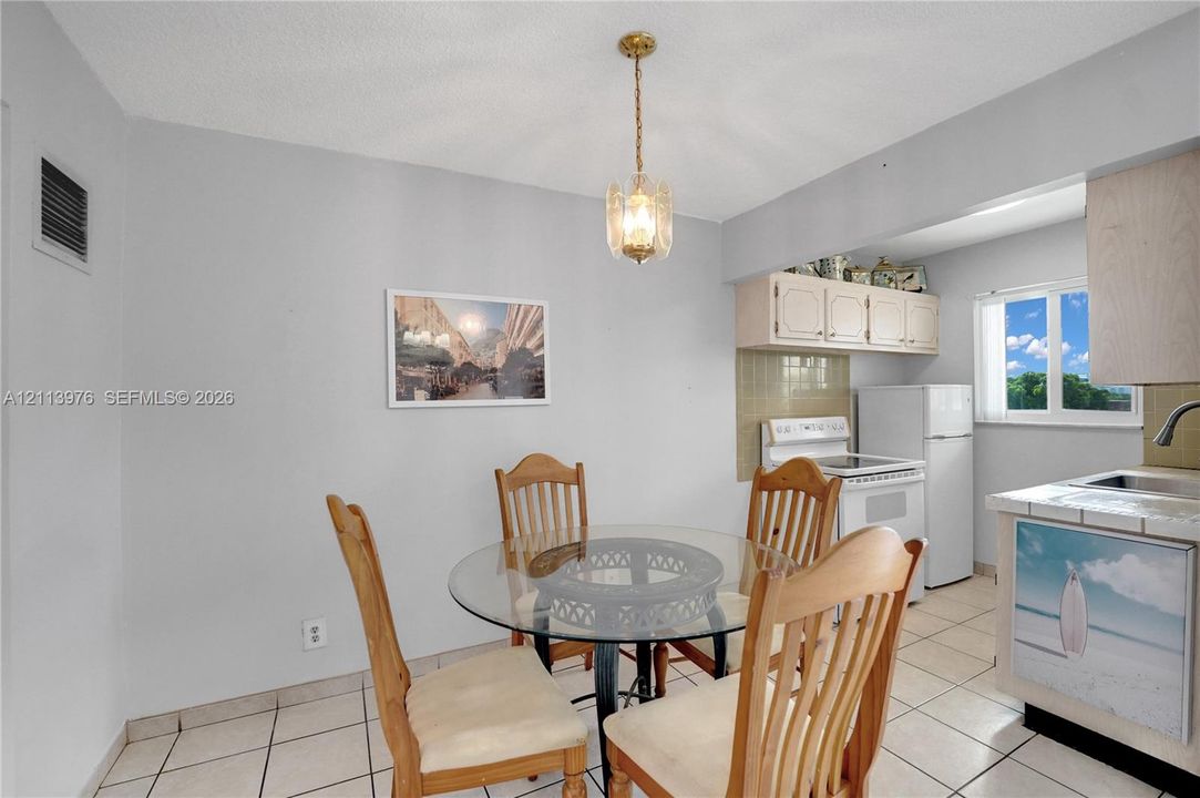 Kitchen area featuring tile flooring, ceiling-mounted decorative pendant lighting, upper cabinetry, and a window