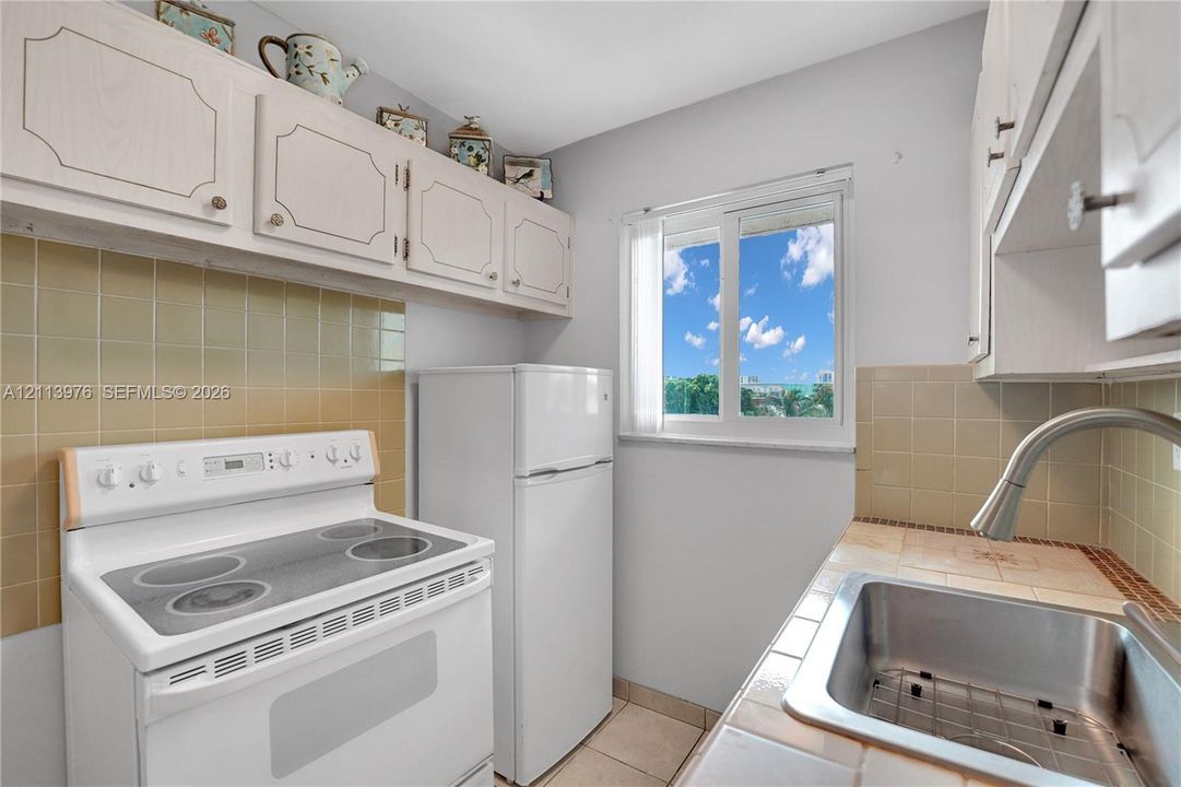 Kitchen featuring white cabinetry, tile backsplash, stainless steel sink with high-arc faucet, electric range, and tile flooring