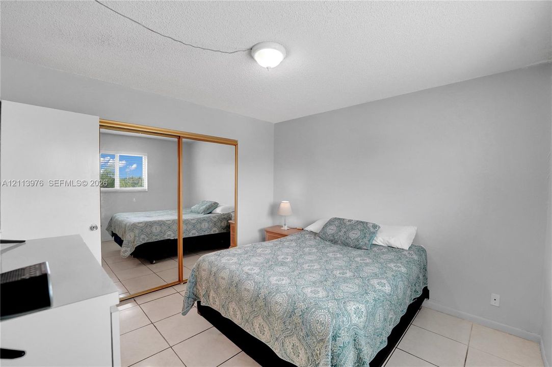 Bedroom featuring neutral wall paint, tile flooring, and a mirrored sliding closet door