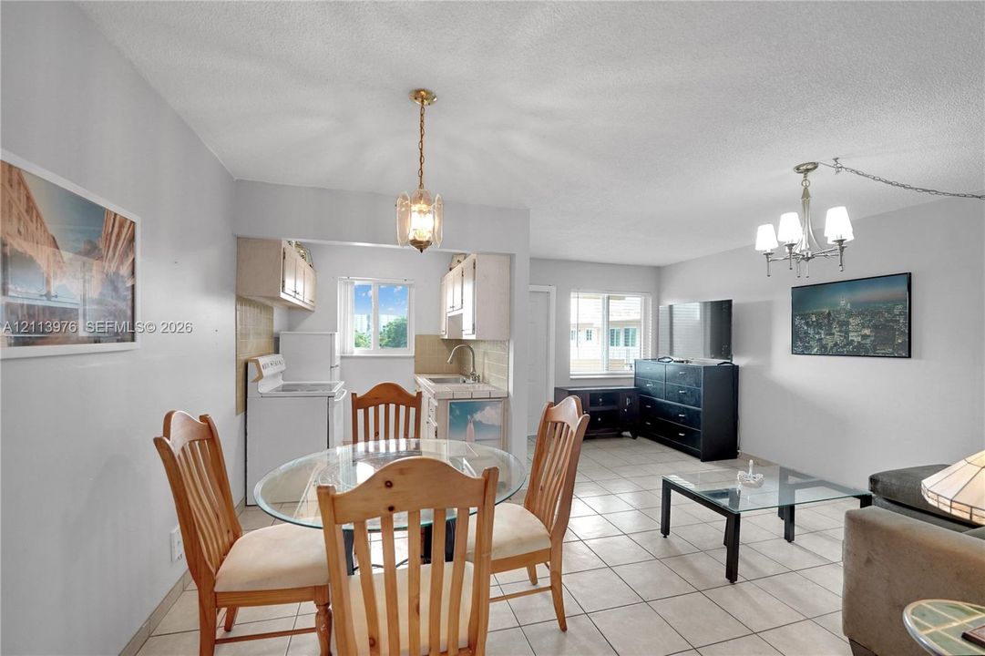 Kitchen area featuring tile countertops, white cabinetry, and a single-basin stainless steel sink, complemented by neutral tile flooring throughout and dual multi-arm metal chandeliers