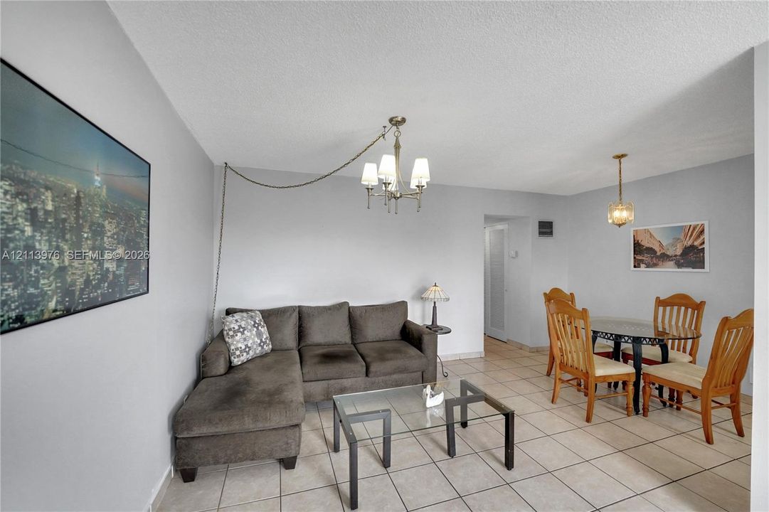 Living area featuring tile flooring, neutral wall paint, and two overhead multi-light chandeliers