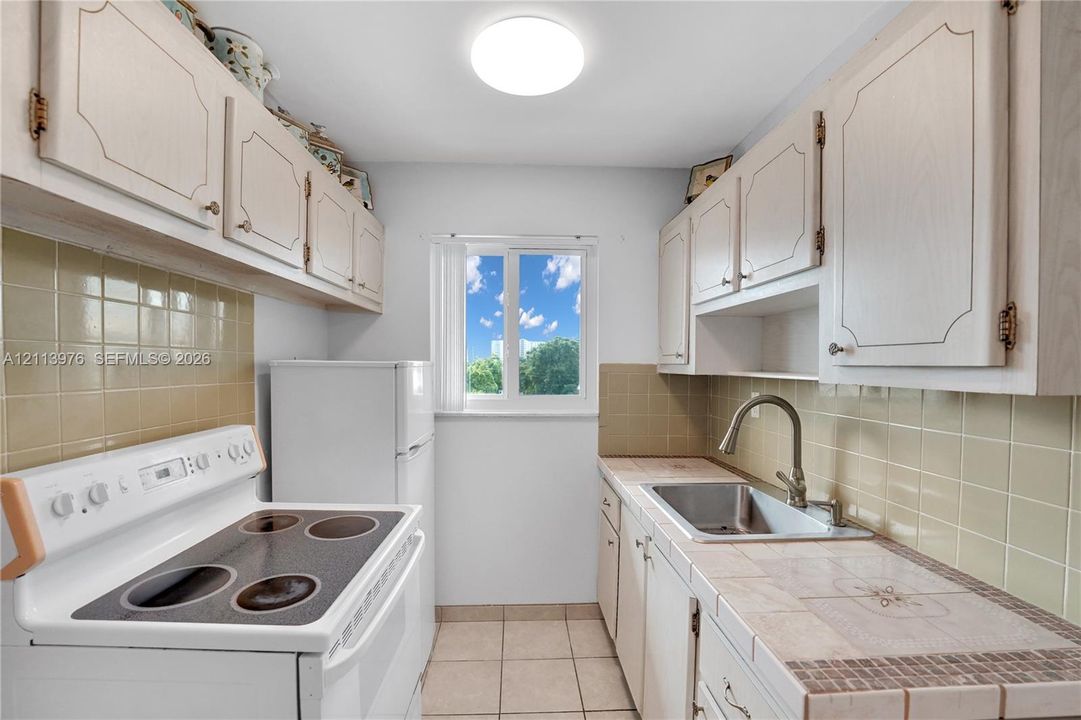 Kitchen featuring white cabinetry, tile countertops, square-tile backsplash, stainless steel sink with high-arc faucet, and ceramic tile flooring