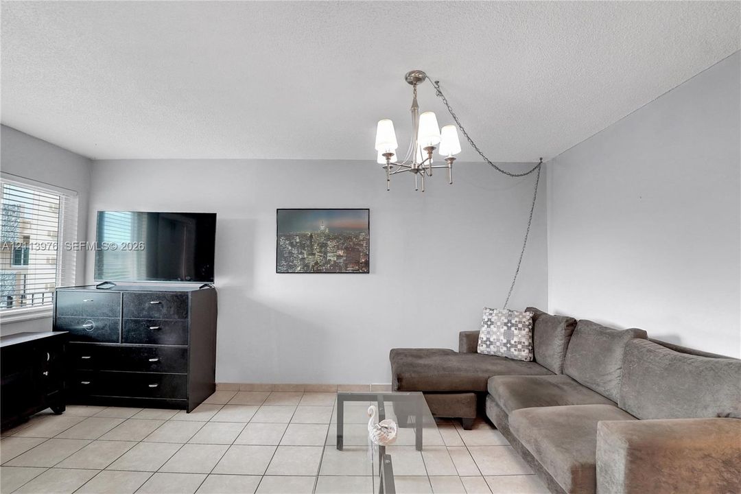 Living area featuring neutral-toned tile flooring, multi-light chandelier, and large window with blinds