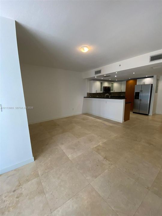 Large-format stone tile flooring, open kitchen peninsula with dark stone countertops, stainless steel refrigerator, and recessed ceiling lighting