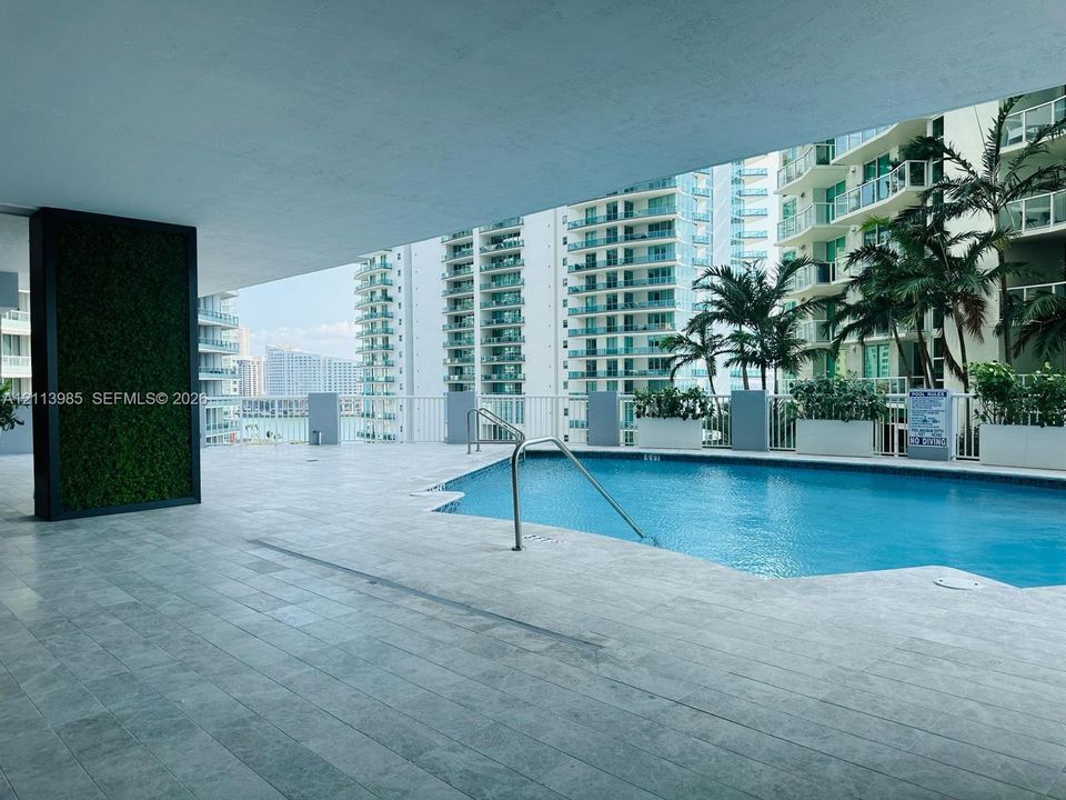 Covered pool deck with stone-tile flooring, metal handrails, integrated greenery wall, and built-in perimeter planters
