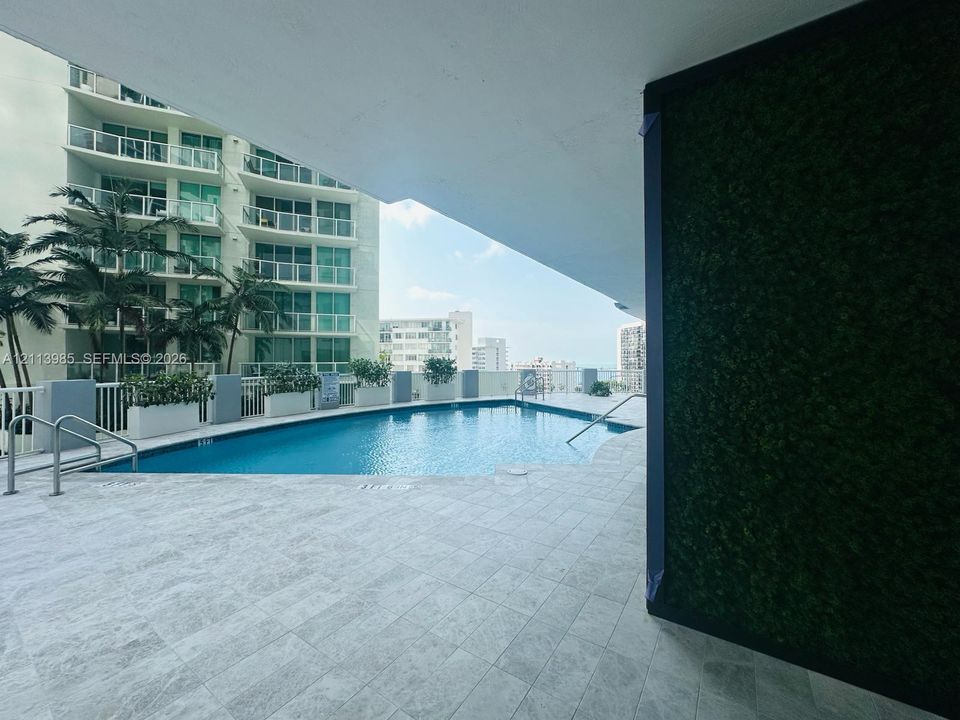 Outdoor swimming pool featuring stone-finish decking, vertical garden wall, and metal safety railings