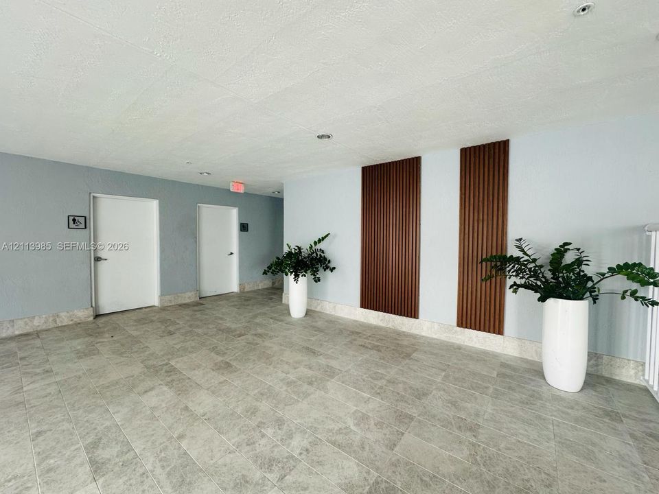 Interior hallway featuring neutral-toned tile flooring, vertical wood-slat wall paneling, and recessed ceiling lighting