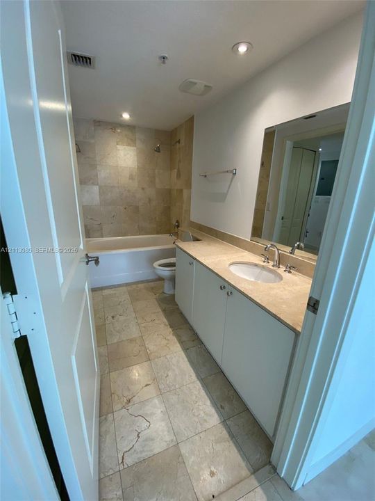 Bathroom featuring large-format tile flooring, tile surround bathtub, white cabinetry, integrated countertop with oval sink, and a wall-mounted mirror