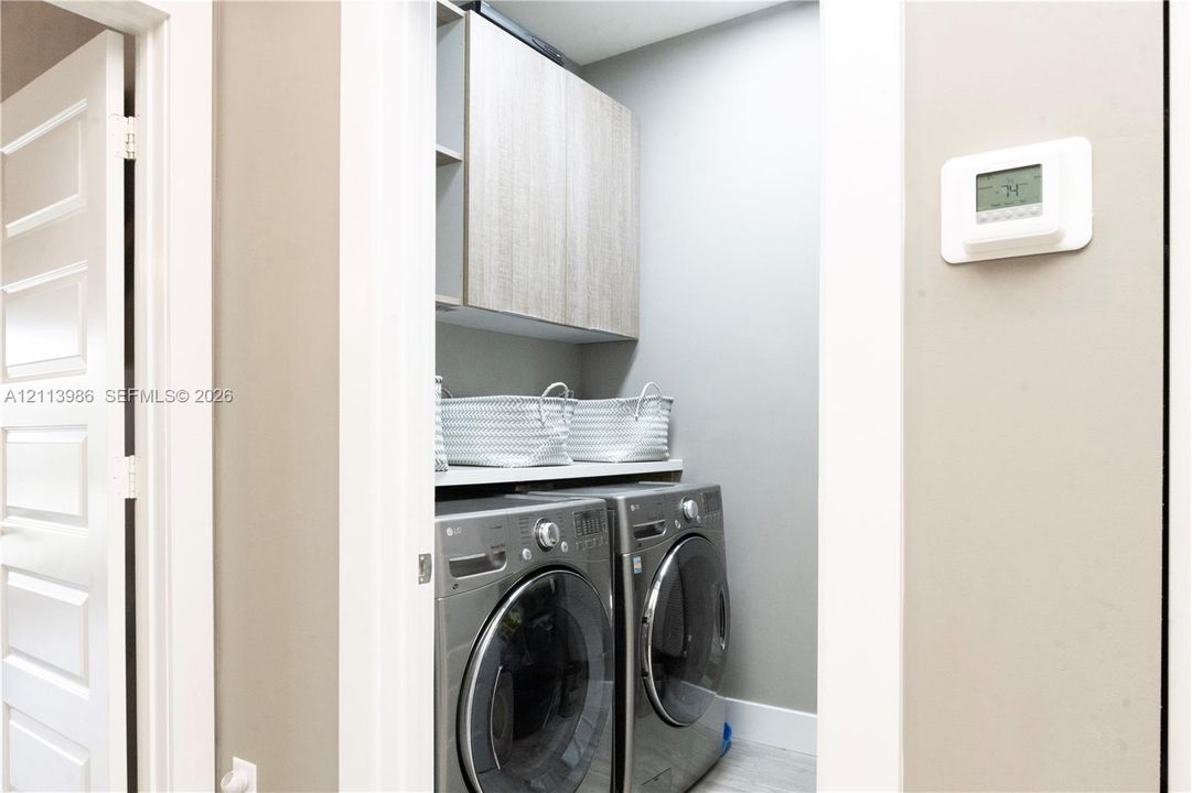 Laundry closet featuring custom wood-finish cabinetry, solid surface shelving, and a wall-mounted digital climate control thermostat