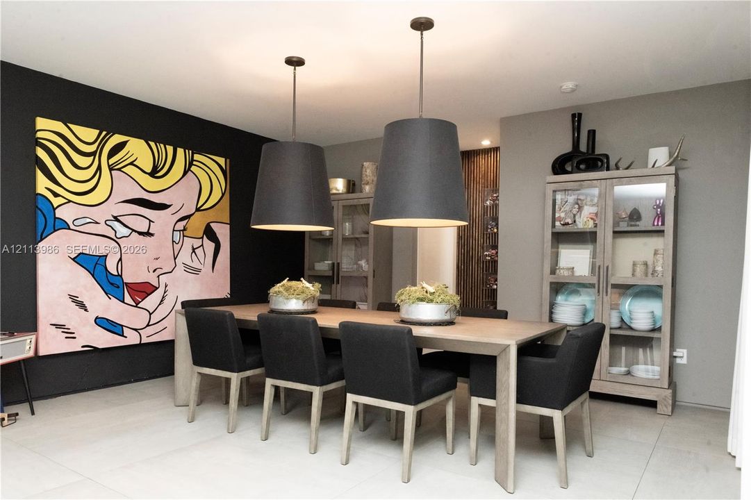 Large-format dining area featuring two suspended black pendant lights, light-toned stone-finish flooring, and a vertical wood-slat accent wall