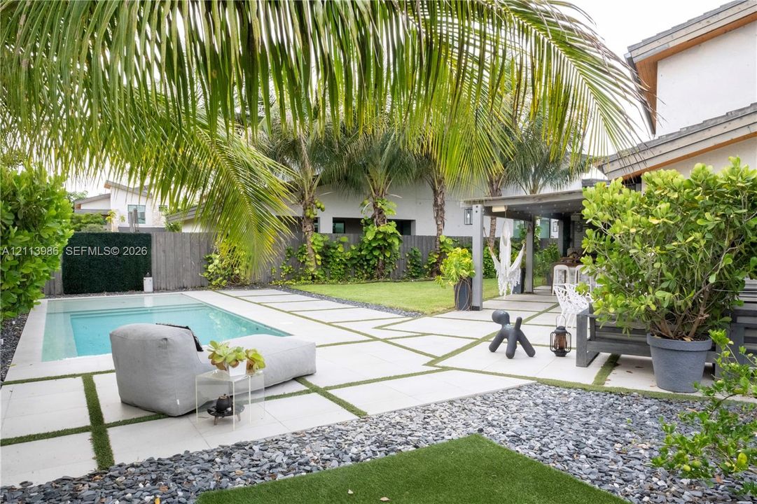 Outdoor living space featuring an in-ground swimming pool, large format concrete pavers with artificial turf inlay, covered patio area, and perimeter landscaping