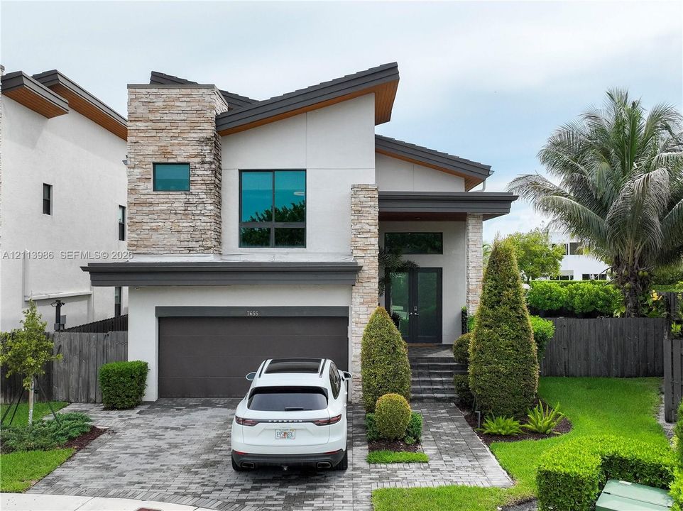 Modern exterior featuring stacked stone accents, smooth stucco finish, multi-level roofline, double-door entry, and a paver driveway