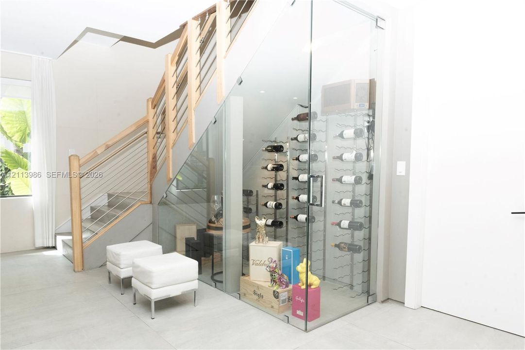 Glass-enclosed wine storage with metal racking, featuring a staircase with wood handrails and horizontal metal cable railing