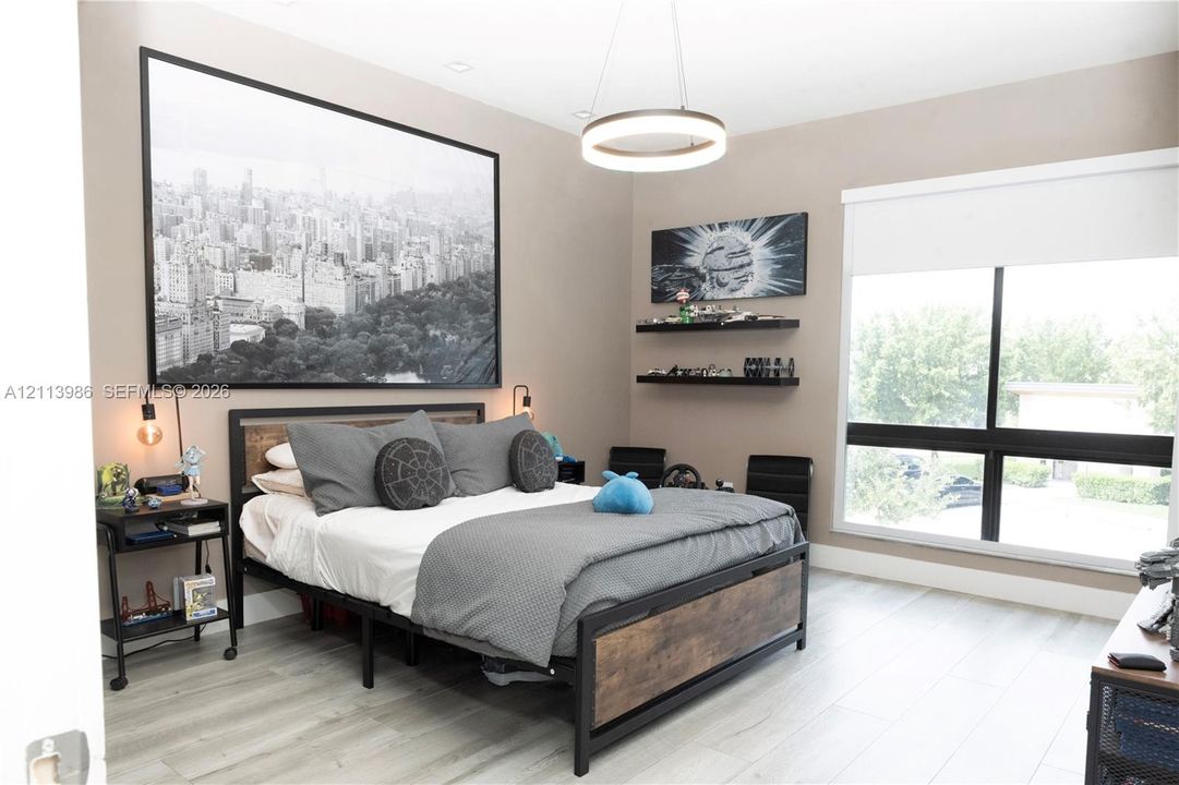 Wood-finish flooring, large window with integrated roller shade, contemporary circular chandelier, and dual wall-mounted floating shelves