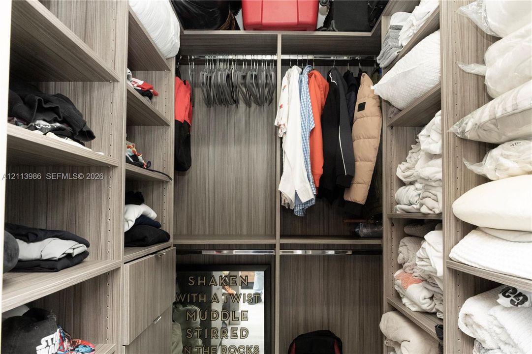 Custom closet system featuring floor-to-ceiling wood-finish shelving, multiple hanging rods, and integrated drawer storage