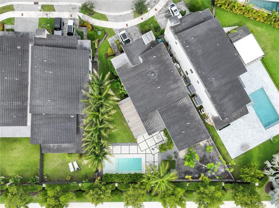 Aerial perspective of a multi-story residence featuring a rectangular swimming pool, integrated hardscaped patio, manicured lawn, and mature perimeter landscaping