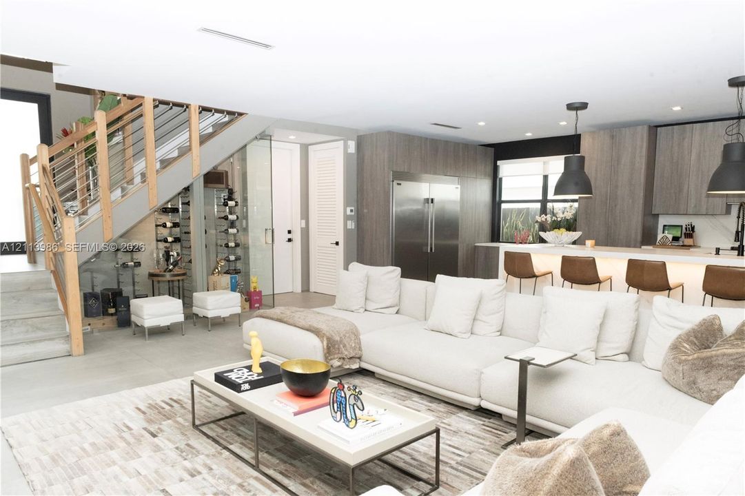Open-concept kitchen featuring flat-panel cabinetry and stainless steel appliances, glass-enclosed wine storage, and a cable-railing staircase with wood handrails