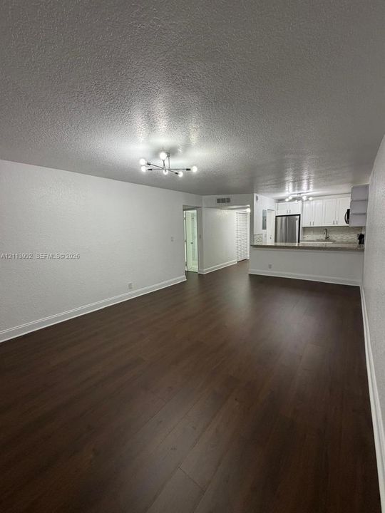 Open-concept interior featuring wood-finish flooring, a contemporary multi-arm chandelier, and a kitchen equipped with white cabinetry, stainless steel appliances, and stone-surface countertops