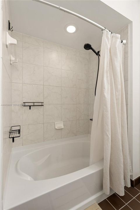 Full-height shower enclosure featuring neutral stone-finish wall tile, an oval-shaped soaking tub, matte black shower hardware, and recessed lighting