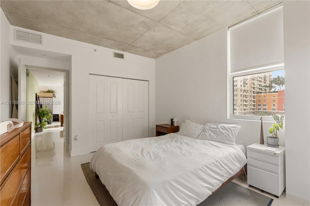 Exposed concrete ceiling, large window with roller shade, double-door closet, and glossy tile flooring