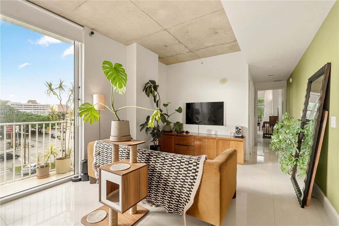 Exposed concrete ceiling, floor-to-ceiling glass sliding door, balcony with metal railing, and polished tile flooring