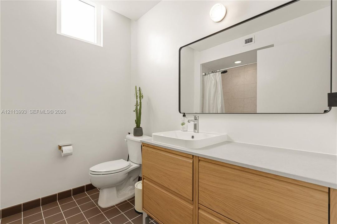 Bathroom featuring a wood-finish vanity with an integrated basin, a large rectangular mirror with a black frame, and tiled flooring