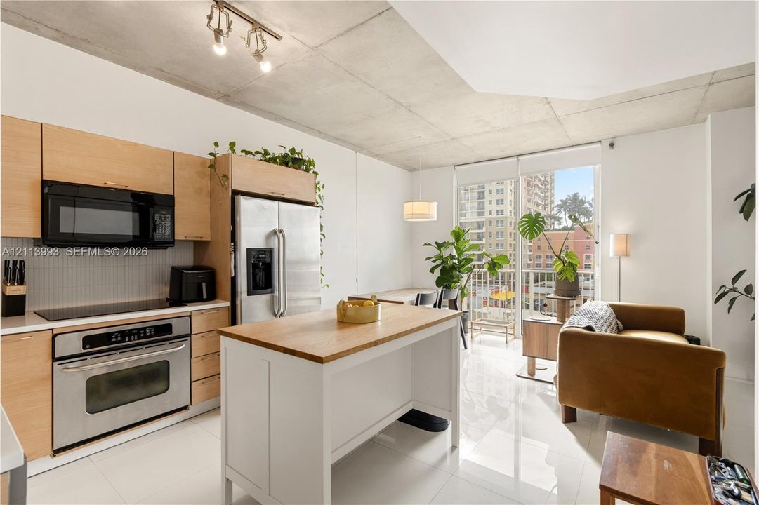 Kitchen featuring light wood-finish cabinetry, stainless steel appliances, a white center island with a wood-finish surface, polished flooring, and exposed concrete ceilings