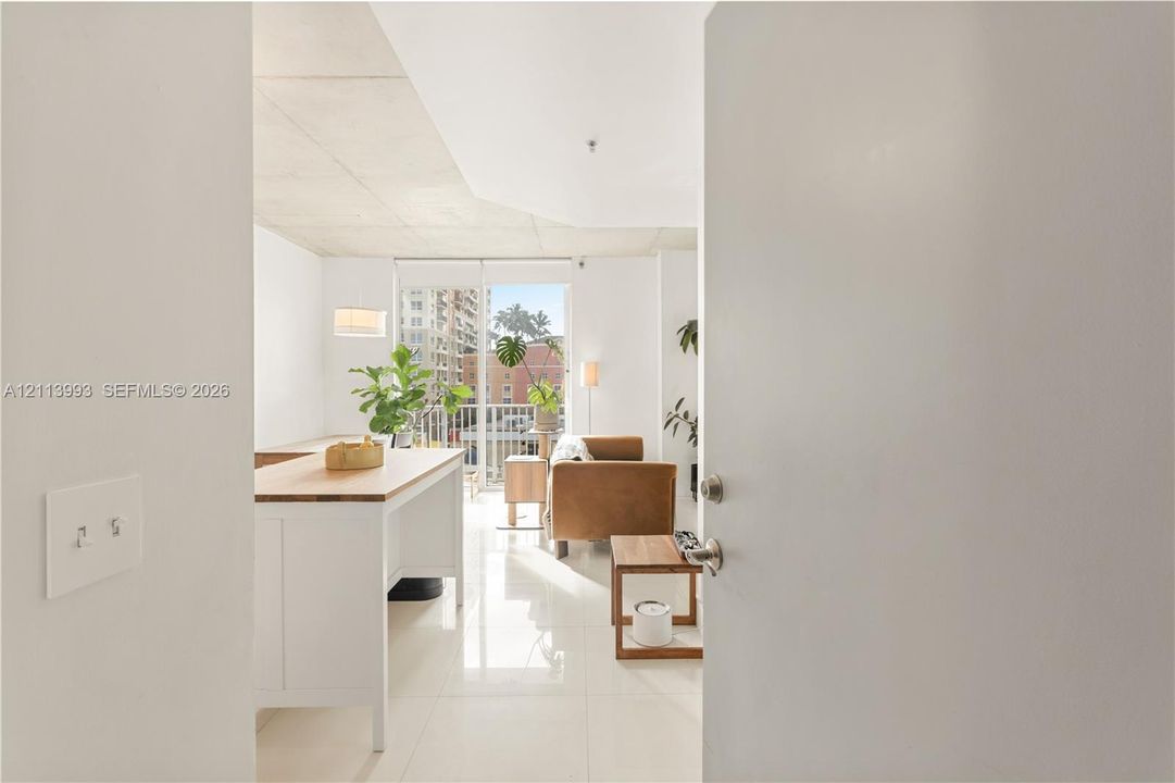 Open-concept living space featuring high ceilings, polished tile flooring, and floor-to-ceiling glass sliding doors opening to a balcony