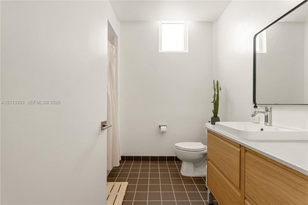Bathroom featuring a wood-finish vanity with a rectangular vessel sink, solid-surface countertop, rectangular mirror with a black frame, and brown tiled flooring
