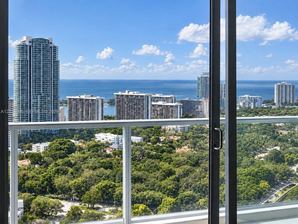 Full-height sliding glass door opening to an exterior balcony featuring a white aluminum railing and expansive metropolitan and coastal scenery