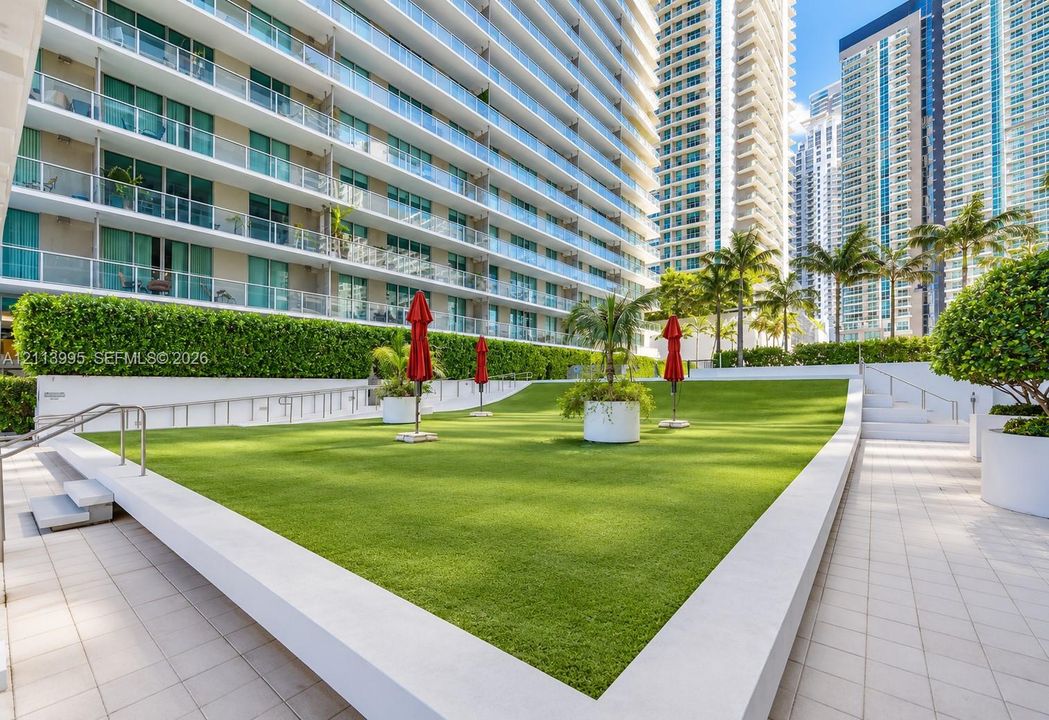 Elevated courtyard featuring synthetic turf, structured manicured hedging, integrated concrete retaining walls, and paved pedestrian walkways
