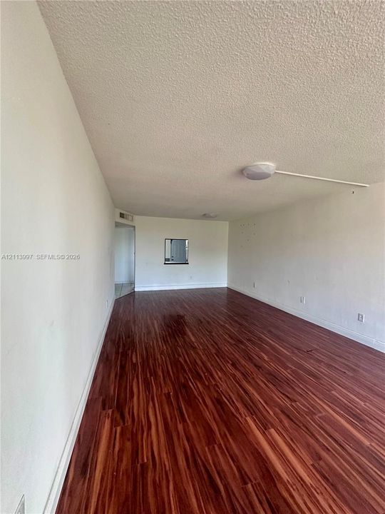 Interior space featuring wood-finish flooring, white walls, a flush-mount ceiling light fixture, and an interior pass-through window