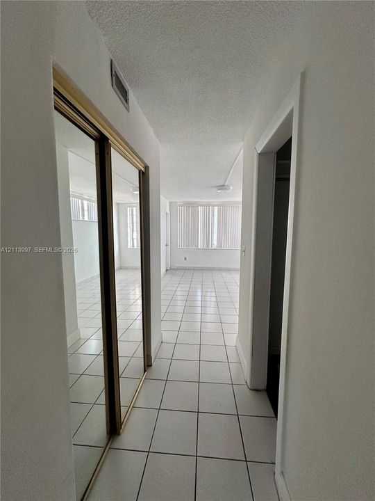Hallway featuring large-format ceramic tile flooring, floor-to-ceiling mirrored closet doors, and smooth-finish ceilings