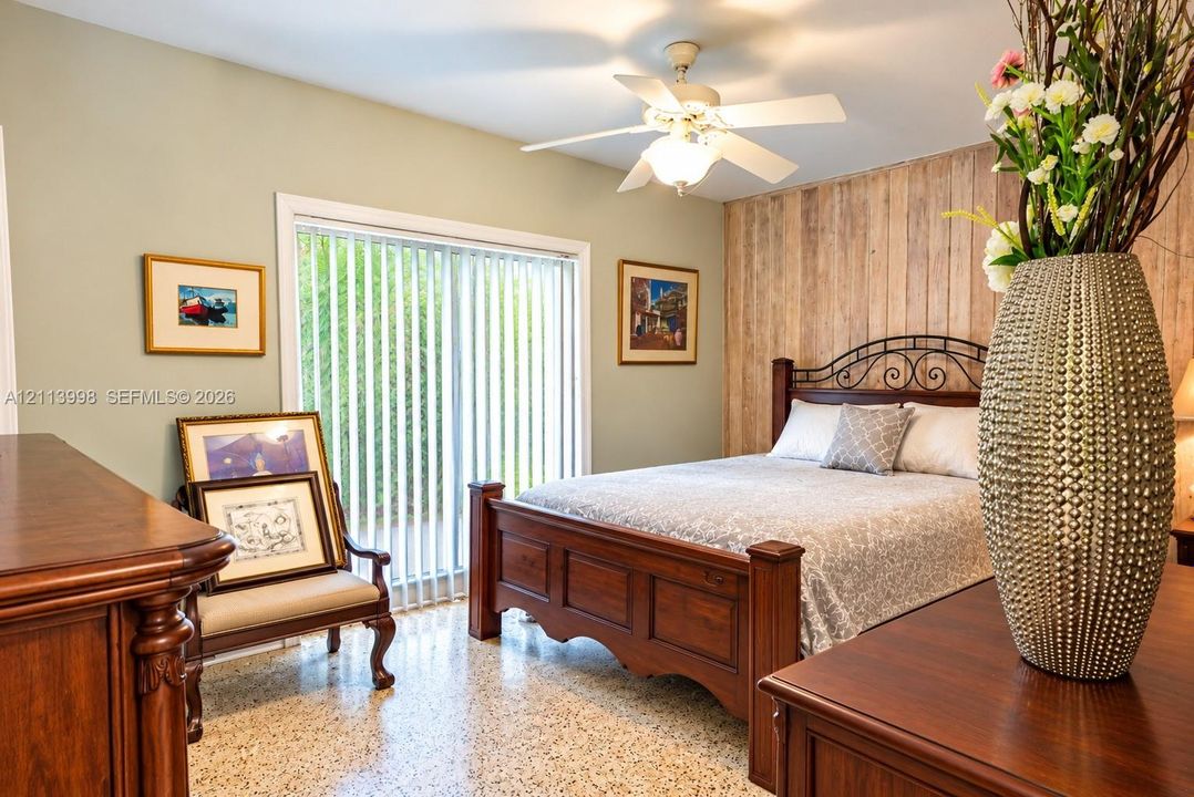 Bedroom featuring a wood-plank accent wall, polished terrazzo flooring, ceiling fan with integrated lighting, and a floor-to-ceiling sliding glass door