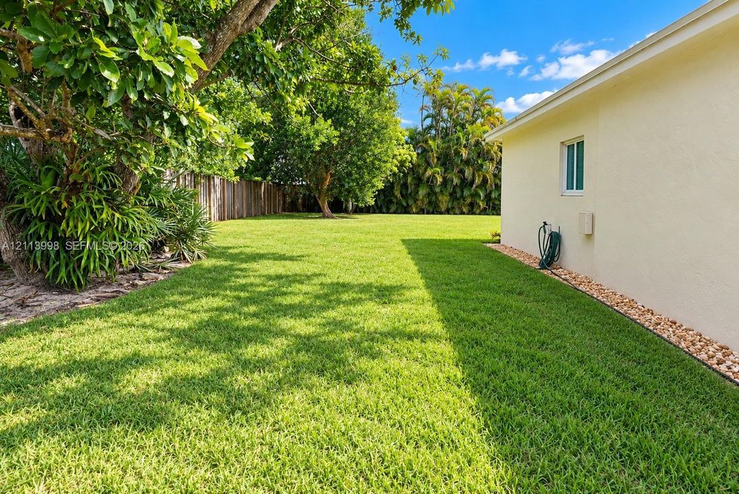 Expansive grassy side yard featuring mature landscaping, wood-tone fencing, and decorative stone ground cover