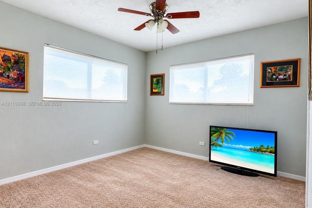 Neutral-toned walls, wall-to-wall carpeting, dual windows with fitted blinds, and a multi-blade ceiling fan with an integrated light fixture