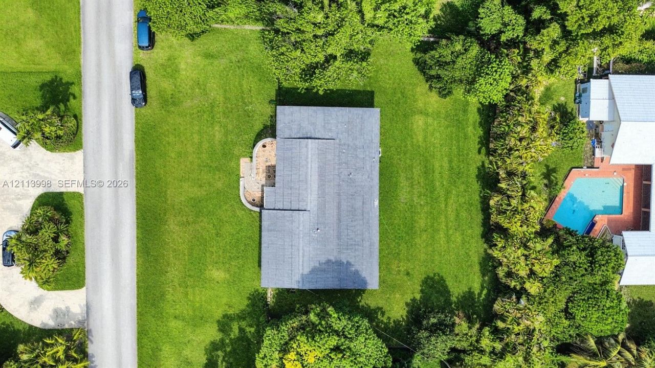 Aerial perspective featuring a spacious lot with mature perimeter trees, expansive lawn, and a paved walkway