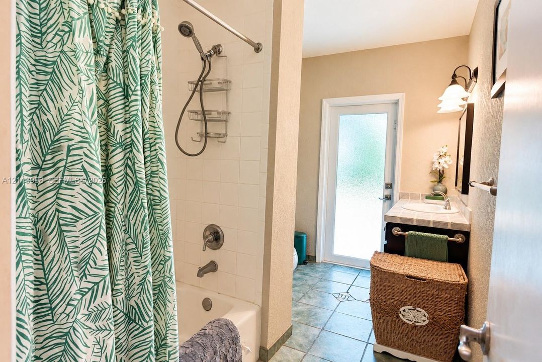 Bathroom featuring a tub-shower combination with tile surround, vanity with tile countertop, ceramic floor tiling, and a glass-paneled exterior door