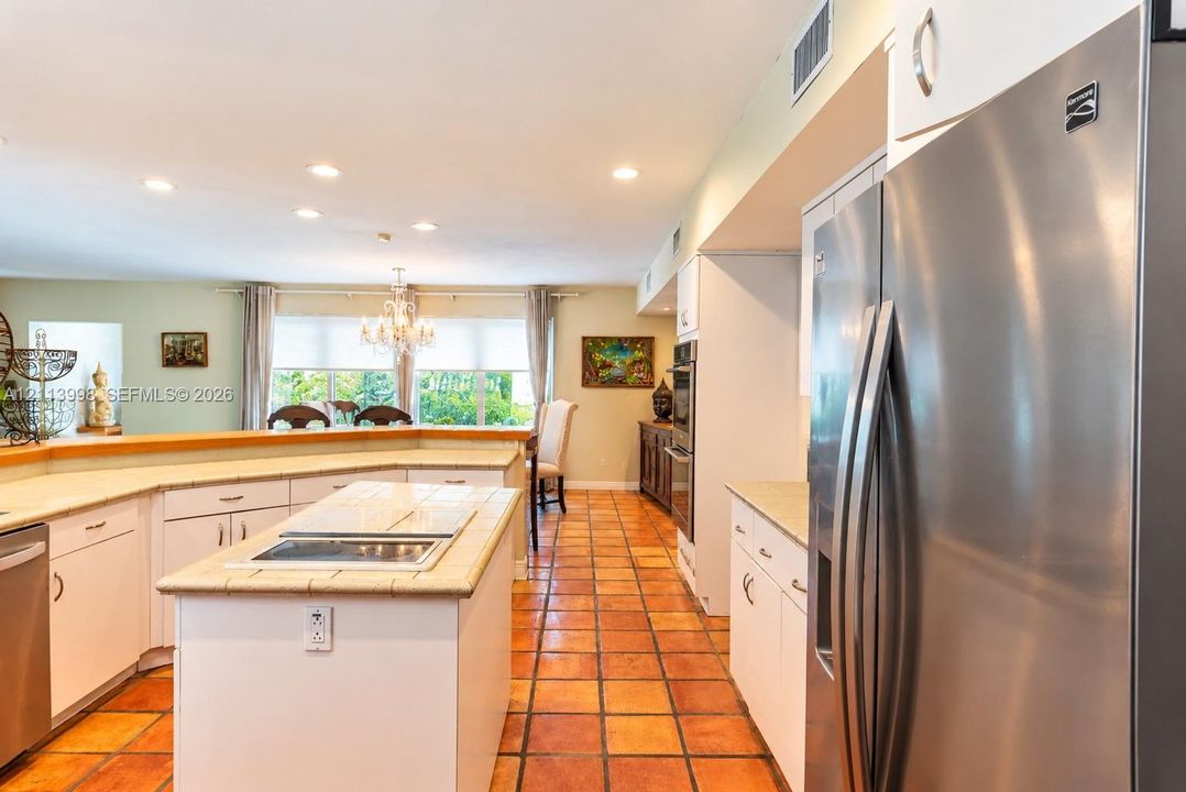Kitchen featuring a central island with a tiled countertop, stainless steel refrigerator, white cabinetry, integrated wall oven, and ceramic tile flooring