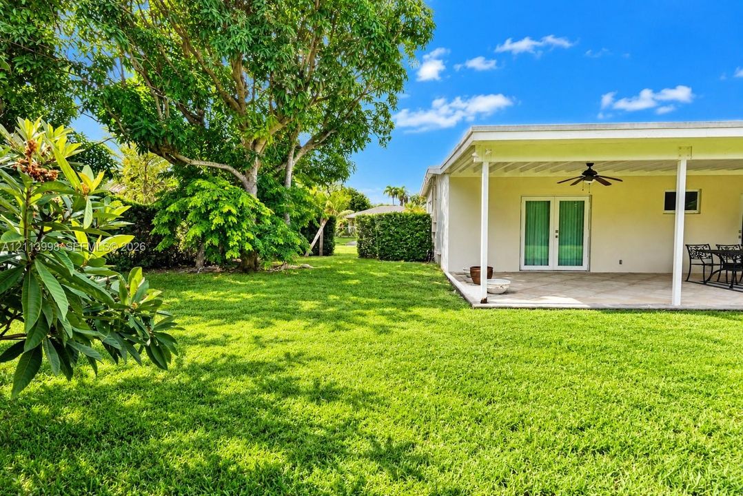 Expansive backyard featuring a manicured lawn, mature trees, and a covered patio with a ceiling fan