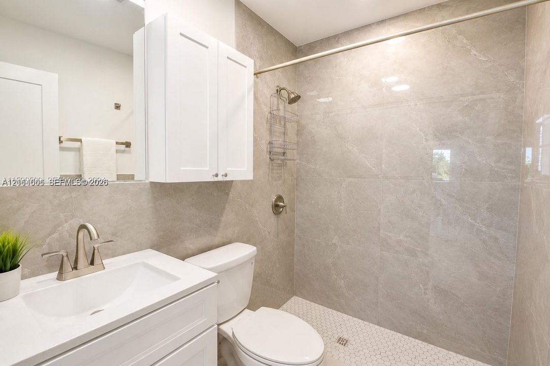 Bathroom featuring large-format gray tiled shower walls, white vanity cabinet with a integrated sink, polished chrome faucet, and geometric tile shower flooring