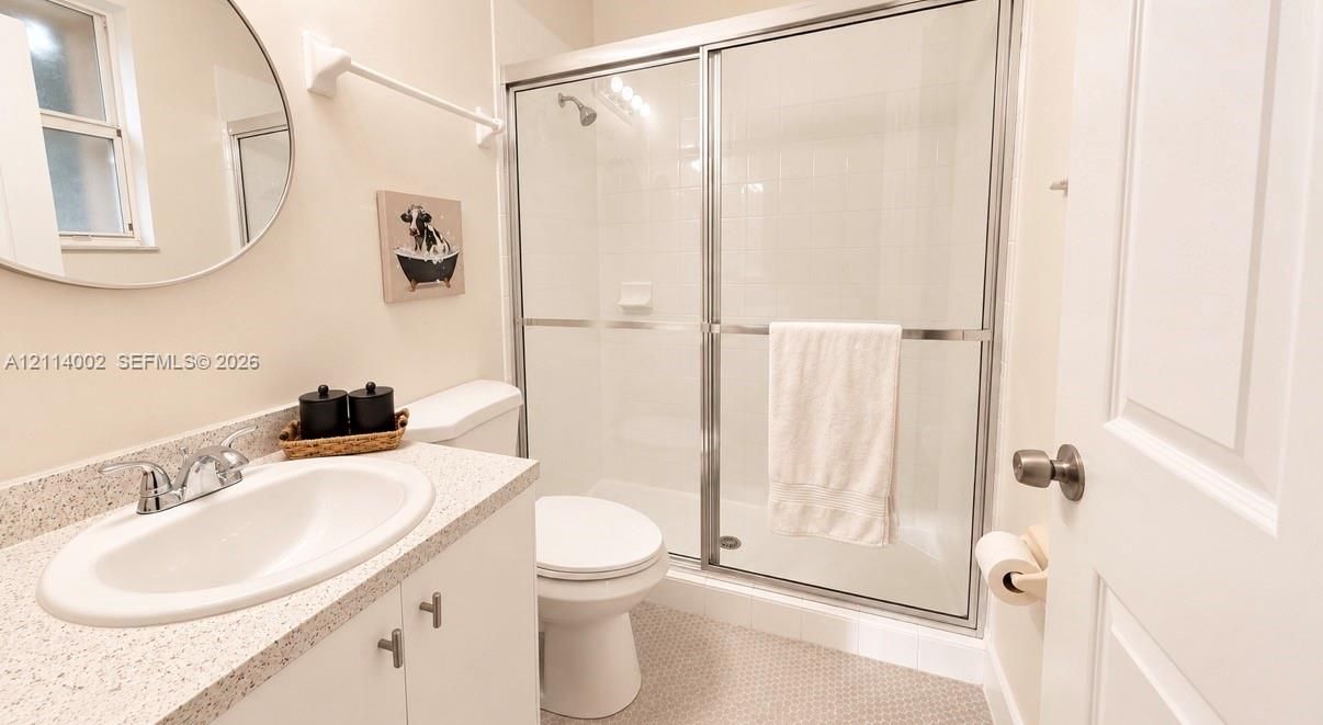 Bathroom featuring a vanity with a stone-composite countertop, oval undermount sink, chrome faucet, circular mirror, and a shower enclosure with sliding glass doors