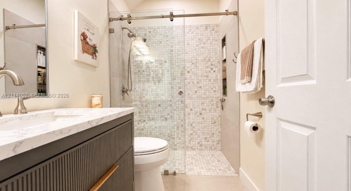 Bathroom featuring a fluted wood-finish vanity with a stone-surface countertop, an integrated sink, a glass-enclosed walk-in shower with mosaic tile accents, and built-in wall shelving